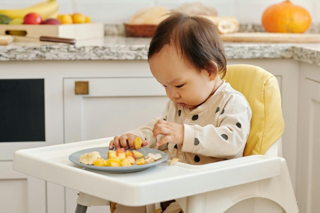 Bebé sentado en una trona comiendo fruta